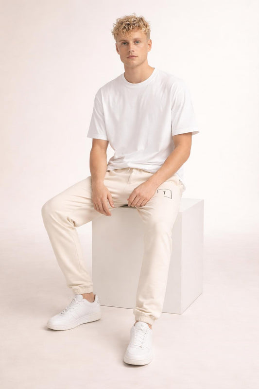 Model sitting while wearing Tovolea Gents Ivory Embroidered Fleece Sweatpants